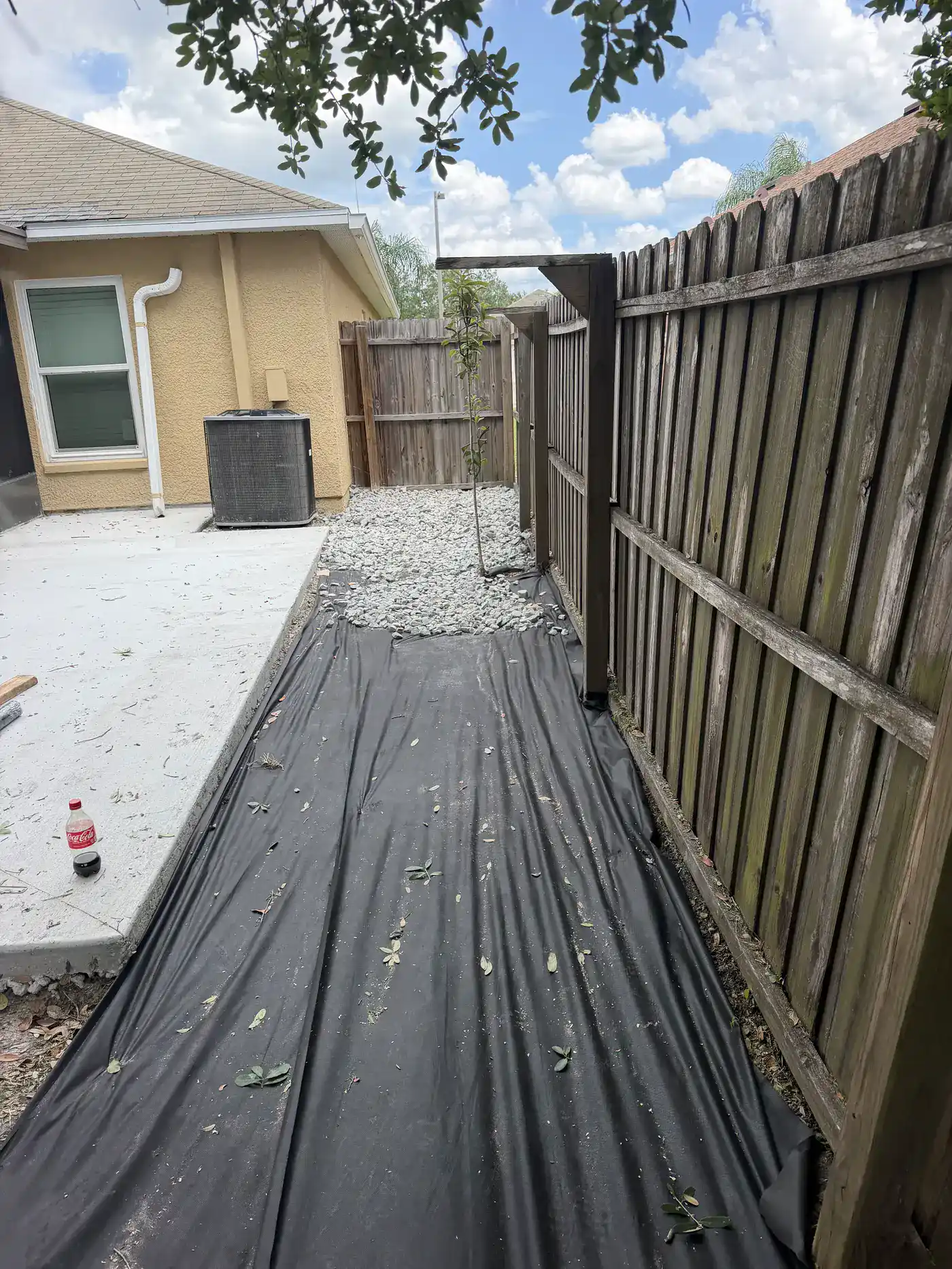 Landscape fabric and gray gravel being prepared along a fenced backyard side passage, Handyman Pros Florida