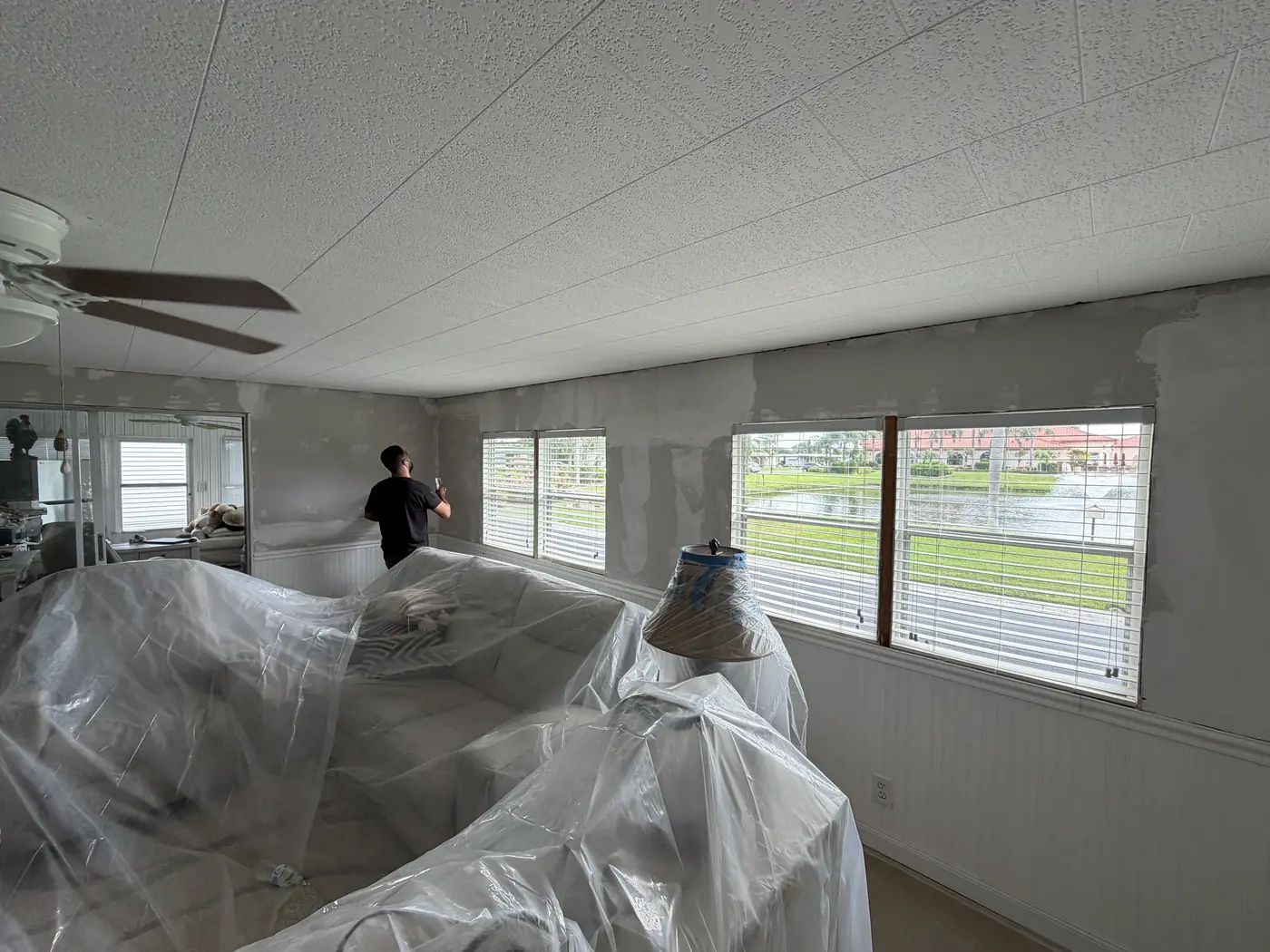 Worker finishing patched drywall in a room protected with plastic sheeting, Handyman Pros Florida