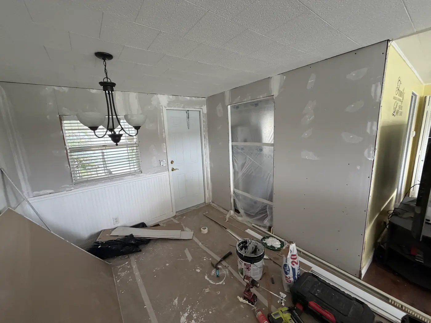 Room under drywall repair with chandelier, masked doorway, and tools on the floor, Handyman Pros Florida