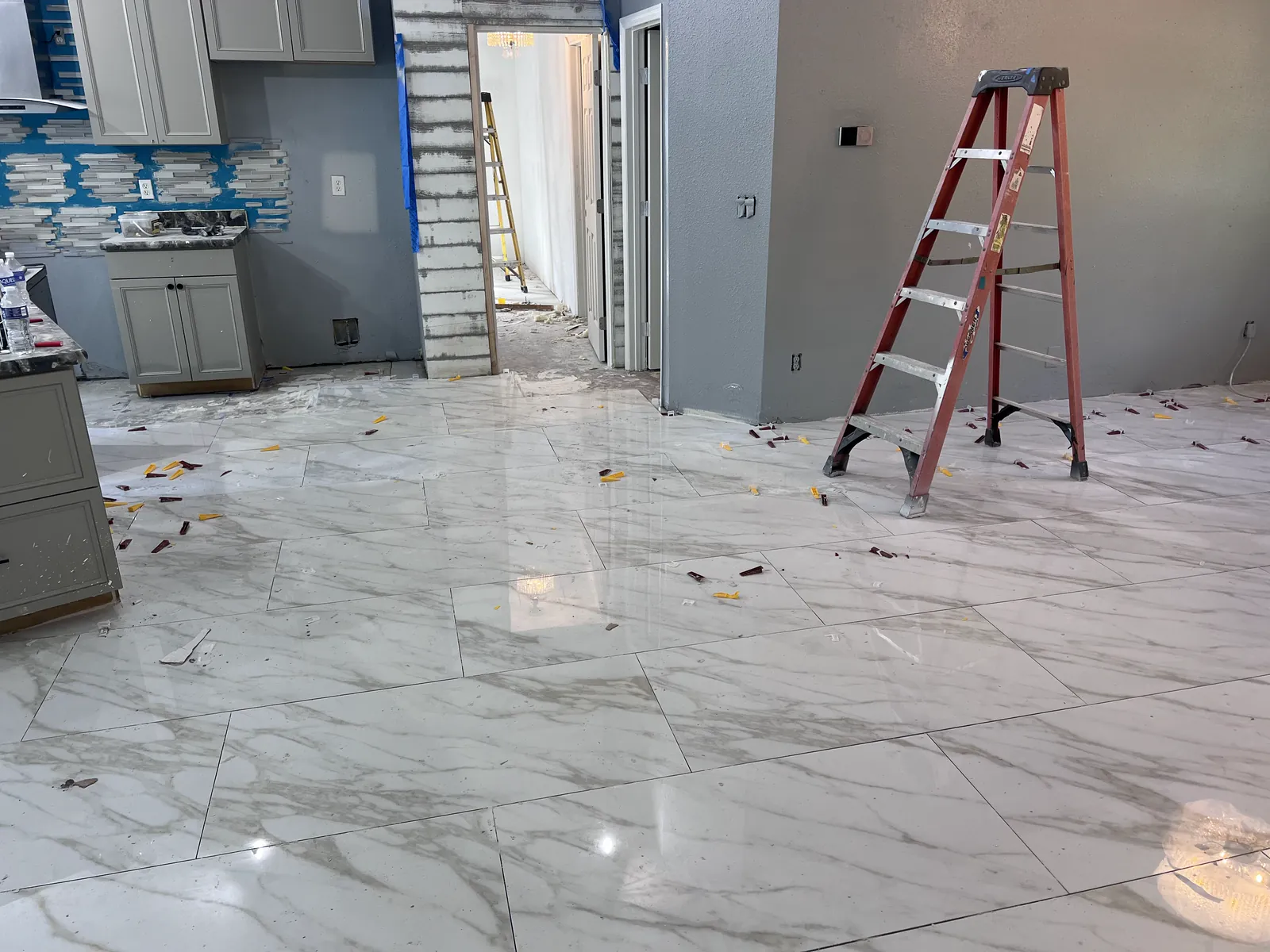 Large light-colored floor tiles installed across a kitchen and living area under renovation, Handyman Pros Florida