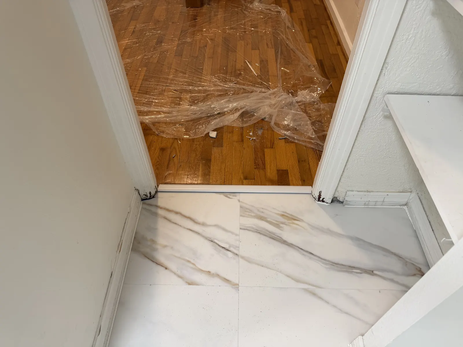 New marble-look porcelain floor tile at a doorway beside protected wood flooring in a Tampa Bay home, Handyman Pros Florida