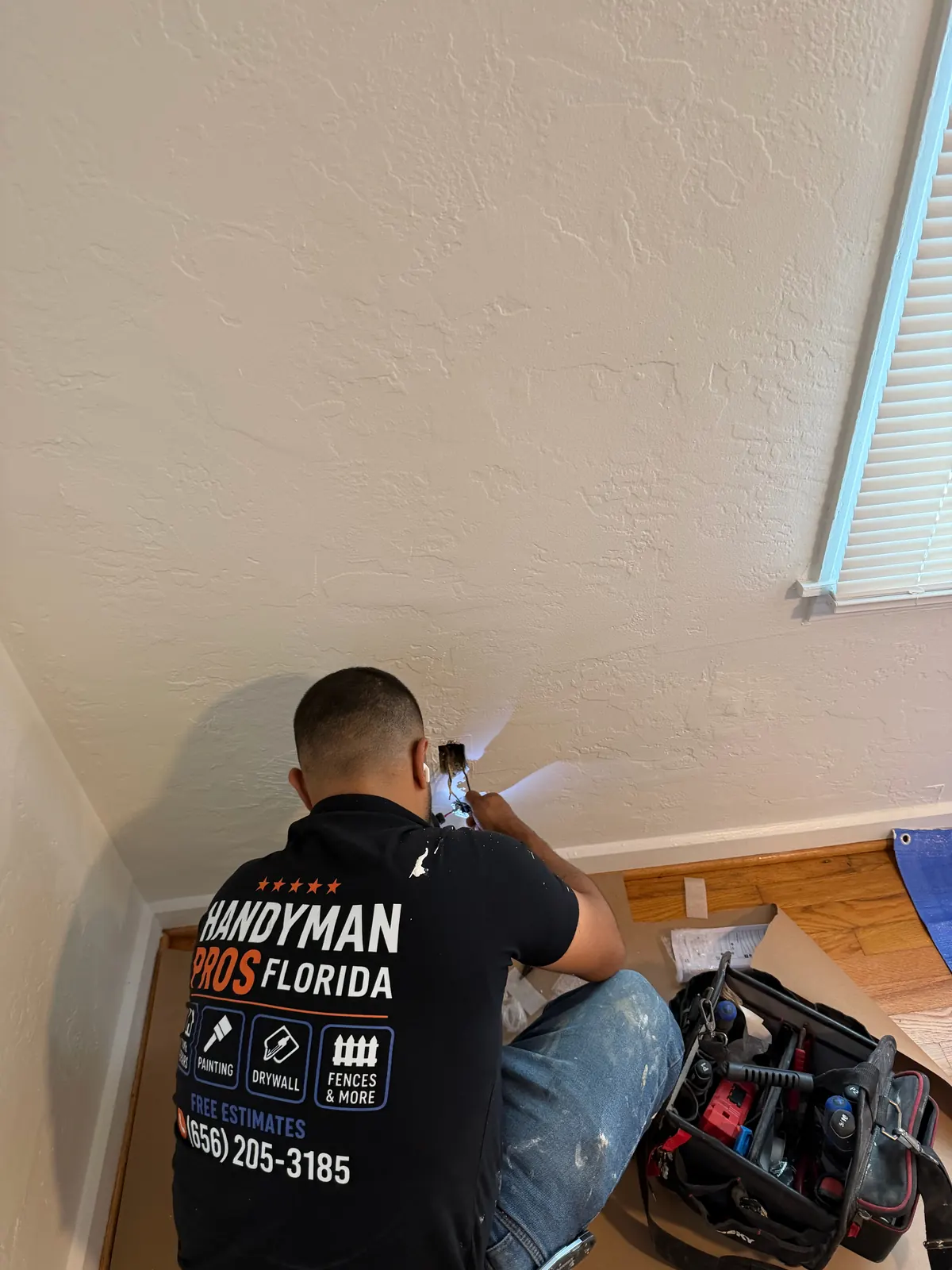 Handyman Pros Florida technician working on a wall outlet box in a Tampa Bay home, shirt showing (656) 205-3185